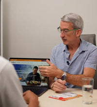 Man sitting at desk showing screen to another person