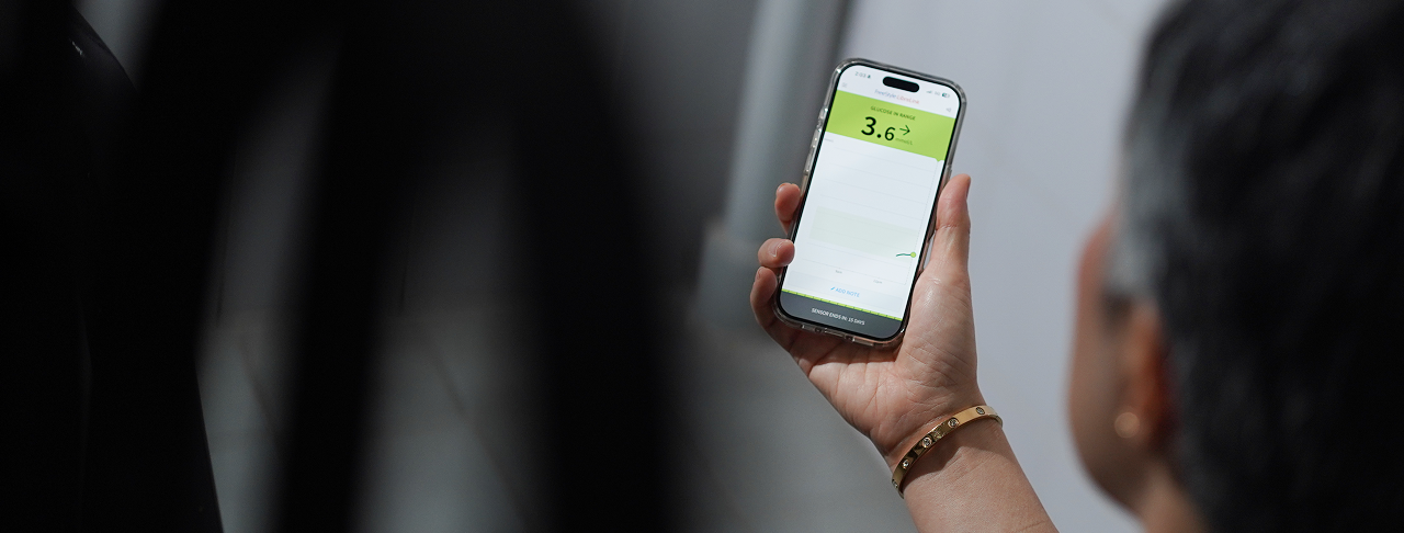 Person holding a smartphone with a green screen displaying '3.6' against a blurred background