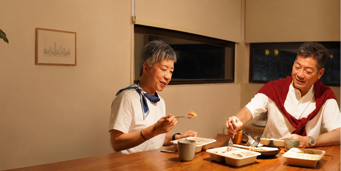 Two people sitting at a table in a home setting, eating together.
